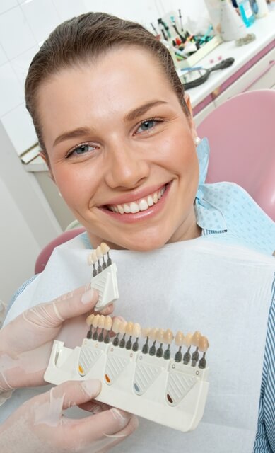 woman smiling, as various options for dental veneer are held up by a dentist