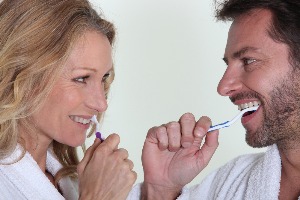 man and women smiling at each other while brushing teeth
