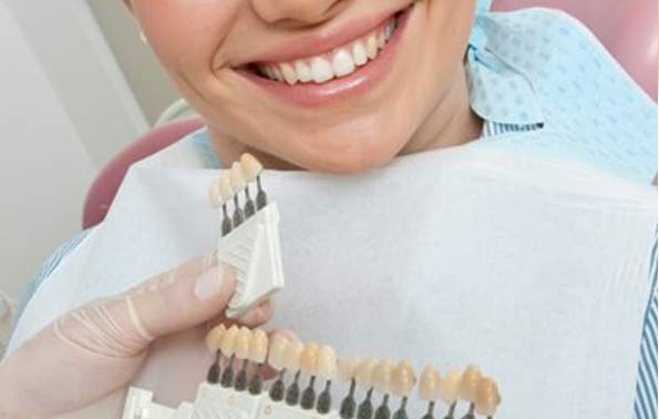 dentist holding veneers up to teeth of smiling patient