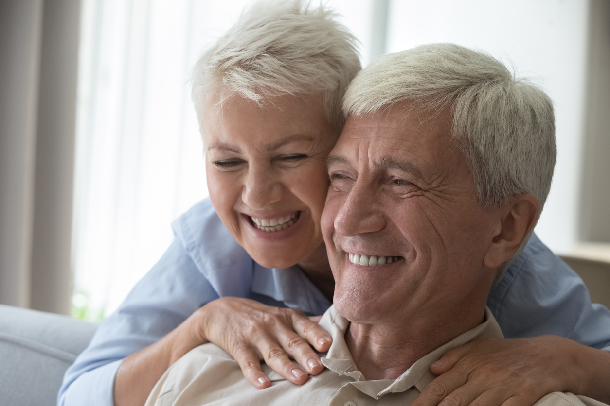 The image shows an older couple smiling to represent the difference between traditional dentures and overdentures.